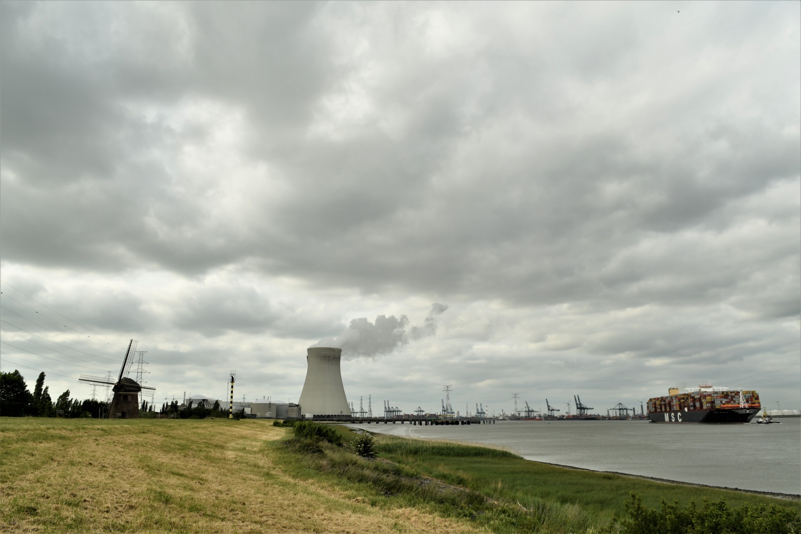Belgium - Doel, ghost city - A windmill.. A nuclear power plant alongside the Schelda river and a portacontainer entering the port of Antwerpen.